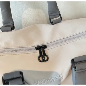 Détail de sac de voyage grand format, tissu beige clair avec sangles grises et zips anneaux.