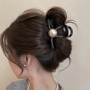 Dettaglio di un'elegante pinza per capelli nera geometrica con una grande perla grigia.