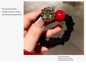 Detailed view of the elegant black hair scrunchie with rhinestone flower and red pearl deco.
