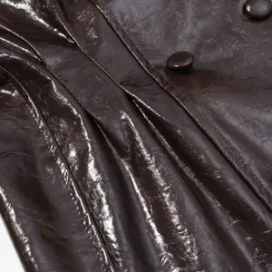 Detalle de piel sintética marrón oscuro brillante, pliegues elegantes y botones a juego.