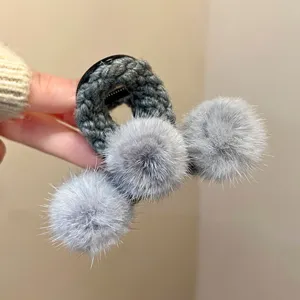 Close-up detail of grey plush hair claw clip with fluffy pom-poms for autumn and winter.