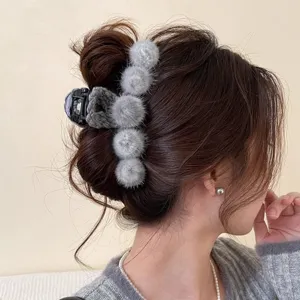 Detail view of a grey plush pom-pom hair claw clip, perfect for autumn and winter styles.