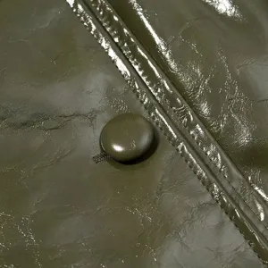 Detalle de chaqueta de cuero sintético brillante verde oliva con botón y finas costuras.