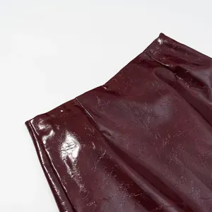 Detalle de piel sintética brillante, textura charol burdeos, primer plano moda mujer.