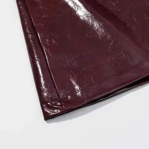 Detalle de falda de cuero burdeos brillante, tejido PU prémium con textura arrugada.