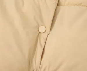 Close-up detail of women's quilted vest fabric texture and snap button in light khaki color.