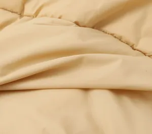 Close-up detail of soft beige quilted cotton vest fabric, showing fine texture and stitching.