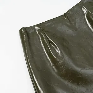 Detalle de prenda de cuero sintético verde oliva brillante, textura suave y brillante con costuras finas.