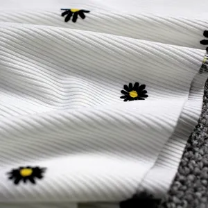Detail view of white ice silk ribbed fabric featuring charming black and yellow daisy patterns.