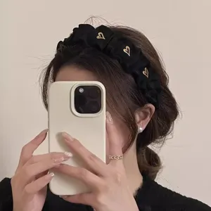 Detailaufnahme des schwarzen gerafften Haarreifs mit goldenen Herzen, Haar-Accessoire.