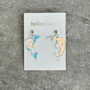 Detailed close-up view of holographic dolphin acrylic earrings on white display card.