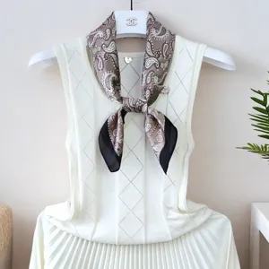 Close-up detail of silky paisley square scarf tied on white knit top, elegant accessory.