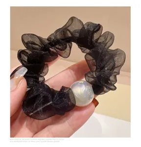Close-up detail van zwarte organza scrunchie met glimmende parel haaraccessoire.