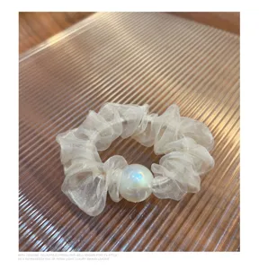 Gedetailleerde close-up van een witte organza haarelastiek met een iriserende parelbedel.