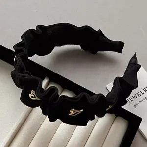 Detailansicht eines eleganten schwarzen Rüschen-Haarreifs mit goldenen Herzakzenten für Damen.