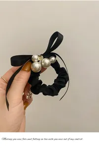 Zwarte satijn haarelastiek met zwarte strik lint en imitatie parels detailweergave.