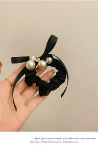 Detailopname van zwarte satin haarscrunchie met parels en strik voor een elegante look.
