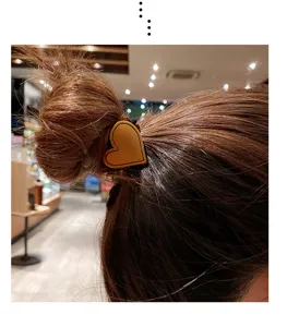 Close-up detail of a chic brown leather heart hair tie worn on a bun, stylish accessory.
