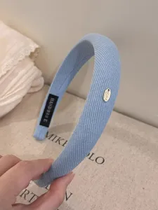 Blaues Stoffhaarband im Detail, mit strukturiertem Textilmaterial und Metallanhänger.