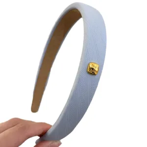 Hellblaue Fischgrät-Haarreif für Damen mit goldfarbenem Akzentlabel. Modisches Haarteil.