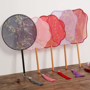 Detail view of traditional Chinese palace fans with gold stamped floral patterns and delicate tassels.