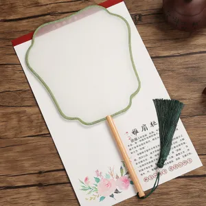 Handmade Chinese round fan detail showing green silk edge, wooden handle, and dark tassel.