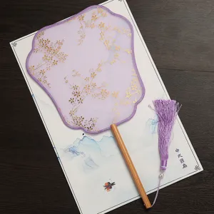 Detail view of a purple Chinese round fan with gold floral pattern, wooden handle and tassel.