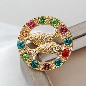 Dettaglio spilla rotonda dorata doppio pesce strass, gioiello di cristalli colorati brillanti.