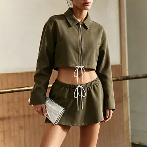 Closeup view of a stylish olive green zip crop jacket and matching low waist mini tennis skirt.