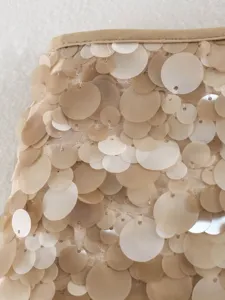Detailed view of women sequin mini skirt fabric texture, elegant nude champagne glitter design.