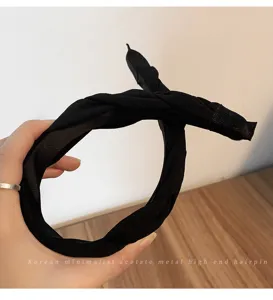 Gros-plan détail d'un serre-tête torsadé en tissu noir minimaliste pour coiffure élégante.