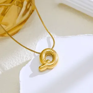 Close-up detail of a gold puff letter Q pendant necklace on white textured background.