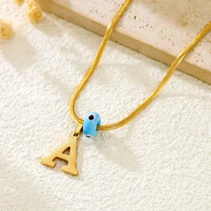 Detailed closeup of a gold snake chain necklace featuring a letter A pendant and evil eye bead.