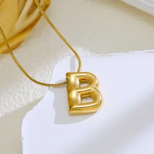 Close-up detail of a stylish gold 3D balloon letter B pendant necklace on white textured prop.
