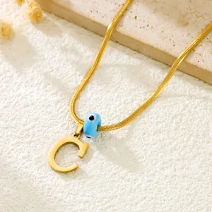 Gold snake bone necklace featuring an initial letter C pendant and a blue evil eye bead detail.
