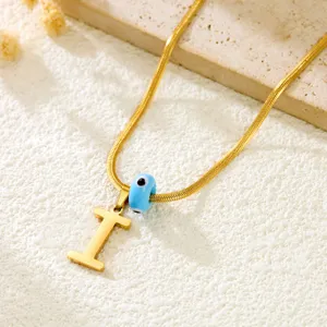 Gold snake chain necklace with letter I pendant and blue evil eye bead detail shot.