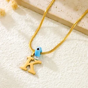 Detailed view of the 14k gold snake chain necklace with letter K pendant and blue evil eye bead.