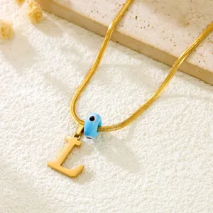Close-up of gold snake chain necklace featuring letter L pendant and evil eye bead.