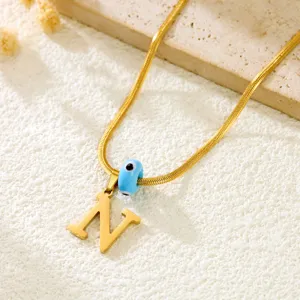 Gold snake bone chain necklace with letter N pendant and evil eye bead for women fashion.