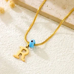 Close-up detail of gold snake chain necklace featuring letter R pendant and evil eye bead.