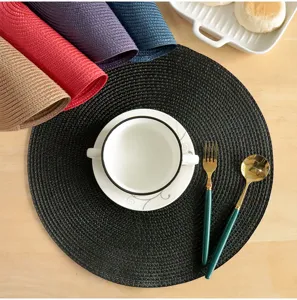 Close-up detail of round woven PP placemat on wooden table with elegant tableware setup.