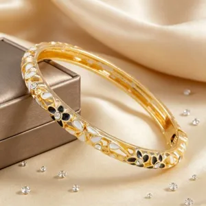 Bracelet jonc en métal doré avec émail floral blanc et noir et incrustation de strass brillants.