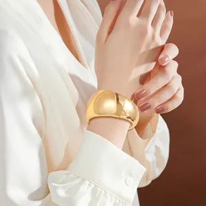 Nahaufnahme eines breiten goldenen Armreifs mit unregelmäßiger Wellenstruktur am Handgelenk.