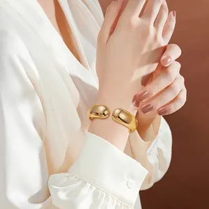 Nahaufnahme des klobigen goldenen Armreifs am Handgelenk mit glaenzender Metalloberflaeche.