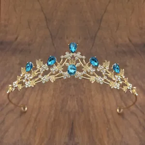 Detailed close-up of golden crystal tiara with blue teardrop rhinestones for kids performance.