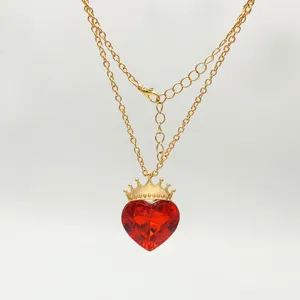 Gold chain necklace close-up, featuring a red crystal heart pendant with a golden crown detail.