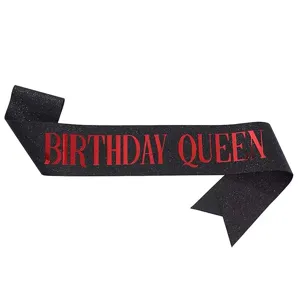 Black glitter birthday queen sash detail shot, sparkling fabric with red text for parties.