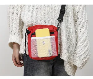Detail shot of red pet training treat bag with mesh pocket and shoulder strap worn outdoor.