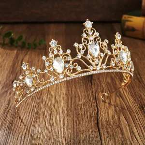 Gold rhinestone crown detail shot, sparkling crystal tiara close-up on dark wooden background.