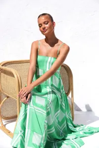 Model wearing a vibrant green and white geometric print summer maxi dress in a rattan chair